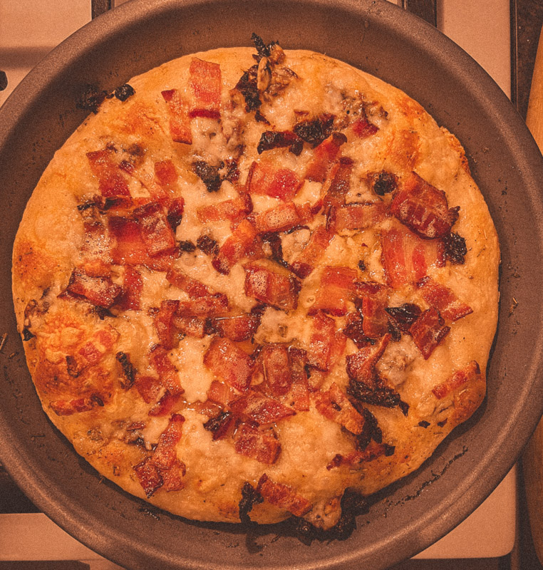 Overhead shot of pizza topped with bacon, sun-dried tomatoes, herb oil, and Havarti.