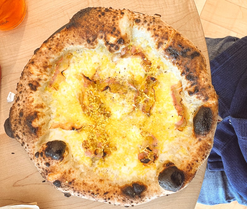 Overhead view of a pizza topped with pancetta, cheese, and grated egg yolk.